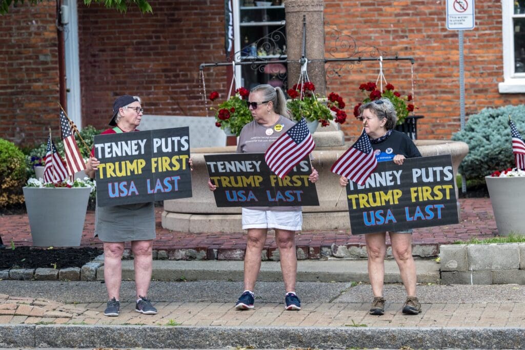Three women holding protest signs against Tenney and Trump
