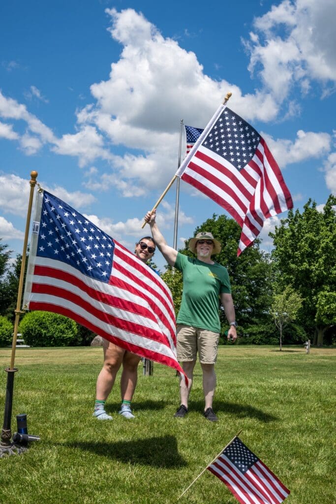 Two people proudly waving large American flags outdoors