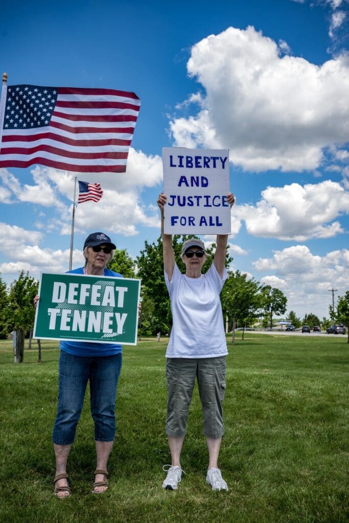 Two women holding protest signs near American flag outdoors