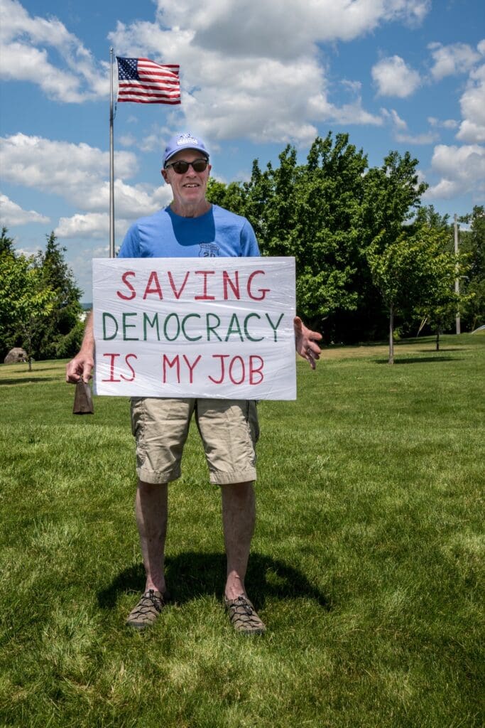 Man holding 'Saving Democracy Is My Job' sign near US flag