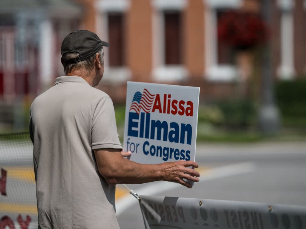 Man holding Alissa Ellman for Congress campaign sign outdoors
