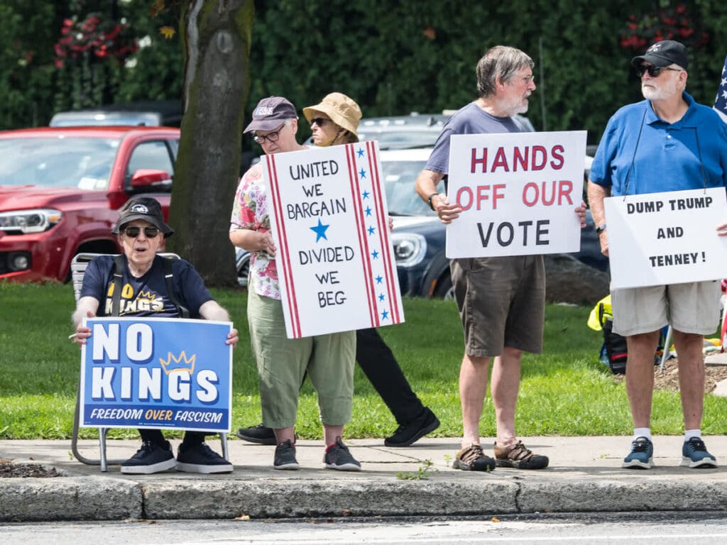Protesters holding political signs including No Kings and Hands Off Our Vote