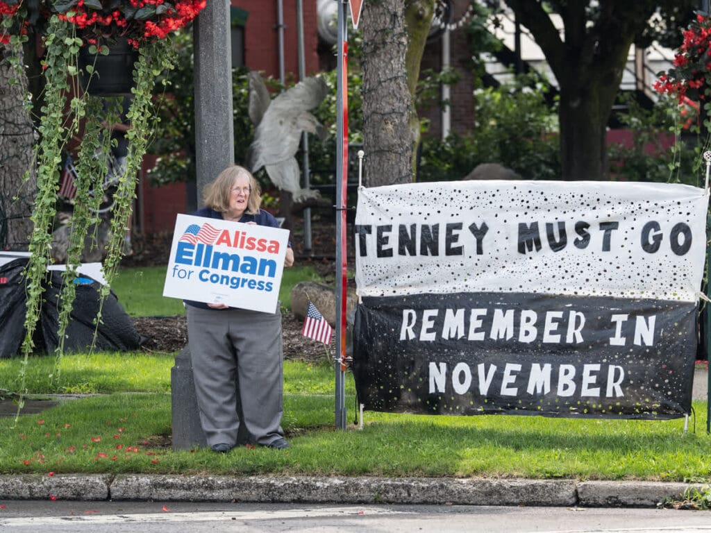 Woman holding Alissa Ellman for Congress sign near protest banner