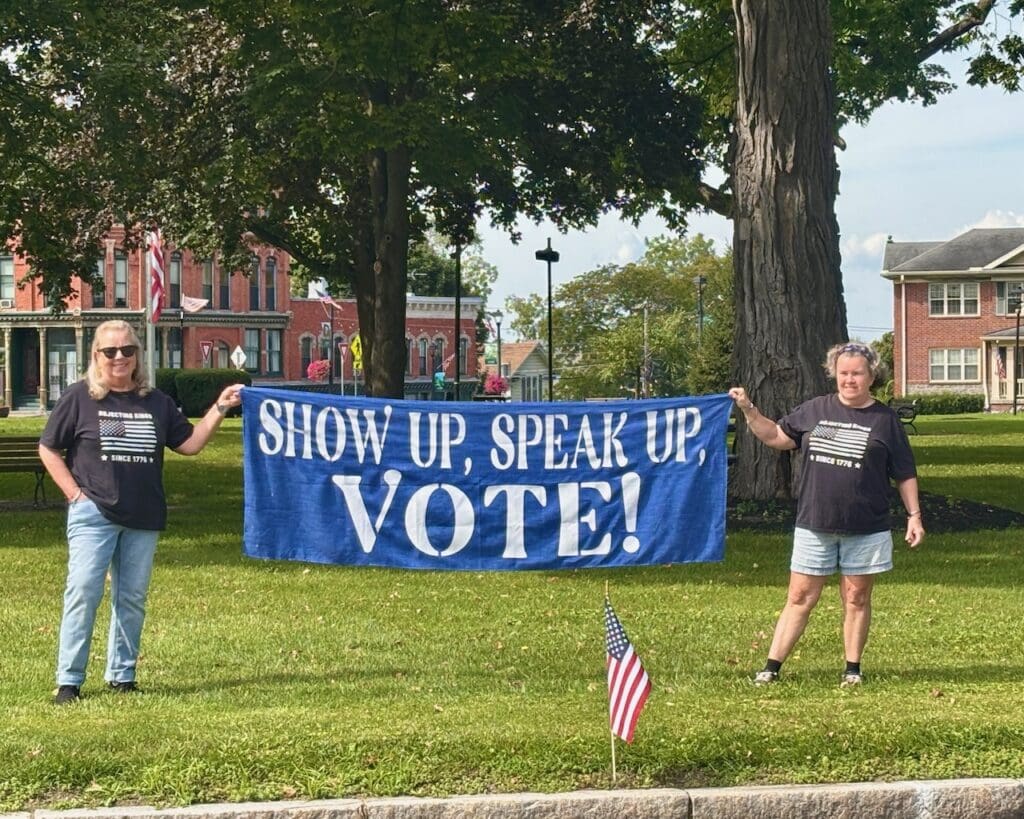 Two women holding a blue Vote banner in a park