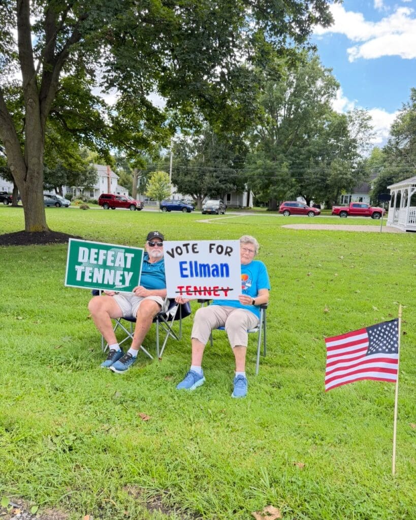 Two people holding campaign signs supporting Ellman and opposing Tenney