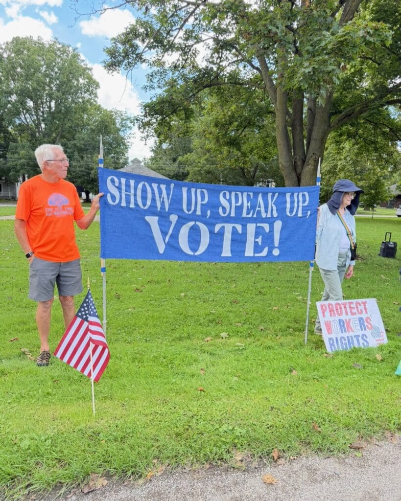 People holding blue banner saying Show Up Speak Up Vote