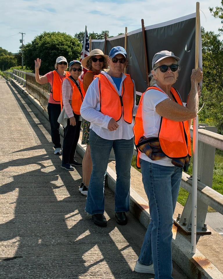 Group of women in orange vests marching on bridge with flags